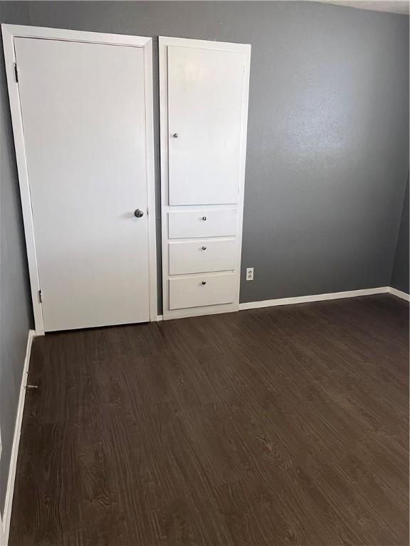 unfurnished bedroom with dark wood-type flooring and baseboards