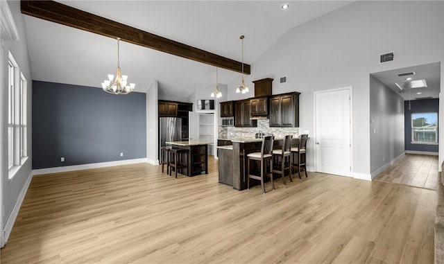 kitchen with hanging light fixtures, light hardwood / wood-style floors, a kitchen bar, dark brown cabinets, and a kitchen island