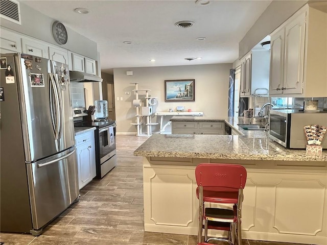 4117 Cork Dr, Corpus Christi, TX 78413 - kitchen with stainless steel appliances, a peninsula, wood finished floors, white cabinets, and under cabinet range hood