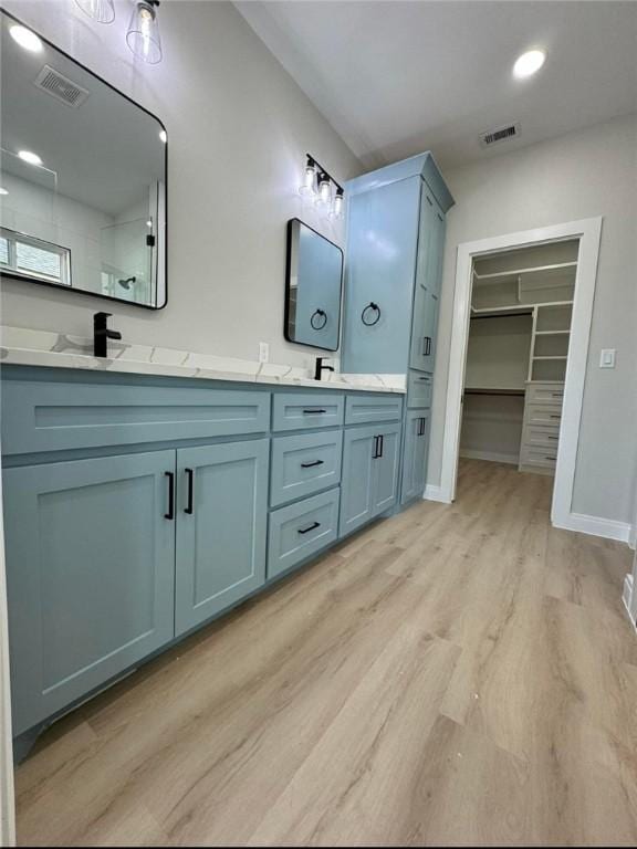 full bathroom featuring double vanity, visible vents, tiled shower, and wood finished floors