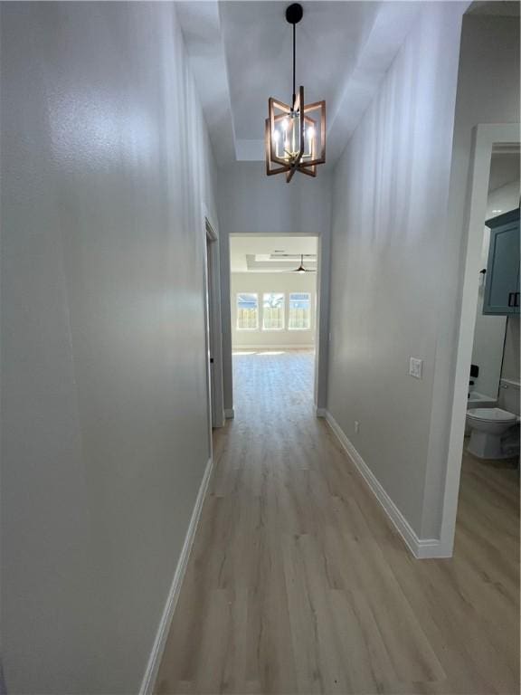 hall featuring a notable chandelier, light wood-style floors, and baseboards