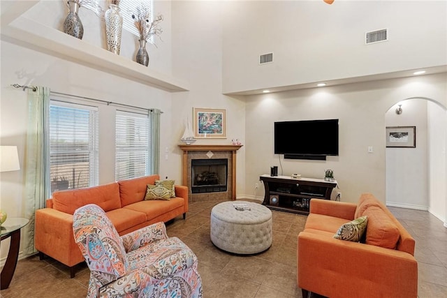 tiled living room featuring a tiled fireplace, visible vents, arched walkways, and a high ceiling