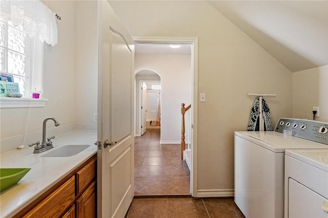 laundry room with arched walkways, a sink, dark tile patterned floors, baseboards, and washing machine and dryer
