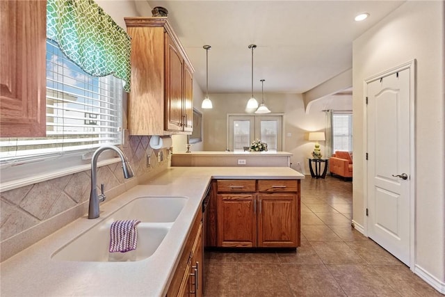 kitchen with brown cabinetry, a peninsula, light countertops, a sink, and backsplash