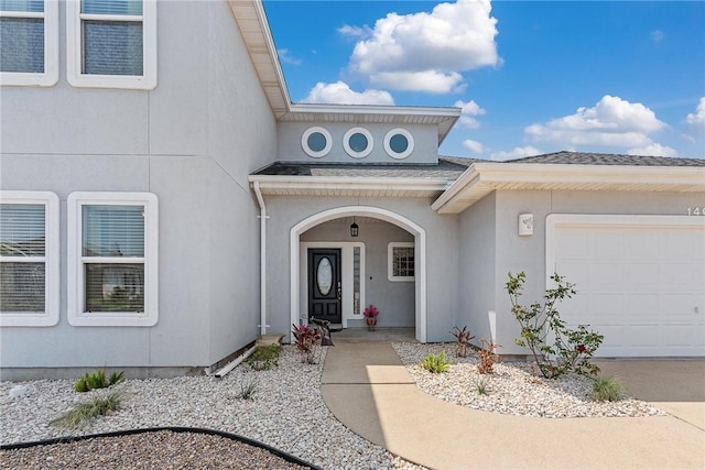 entrance to property featuring a garage, stucco siding, and a shingled roof
