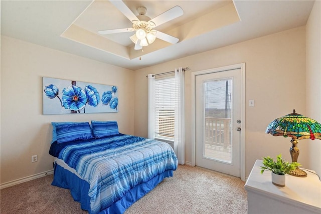 bedroom with a tray ceiling, access to exterior, carpet floors, and baseboards