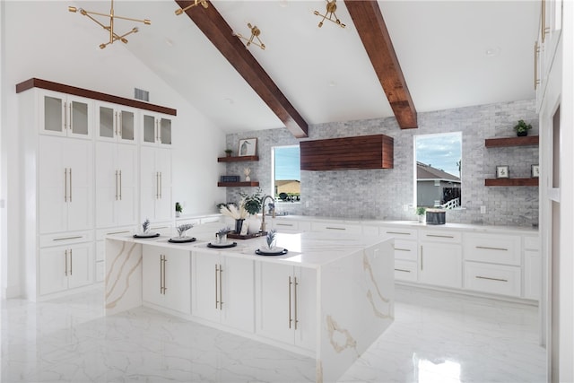 kitchen featuring white cabinets, a kitchen island with sink, light stone counters, and backsplash