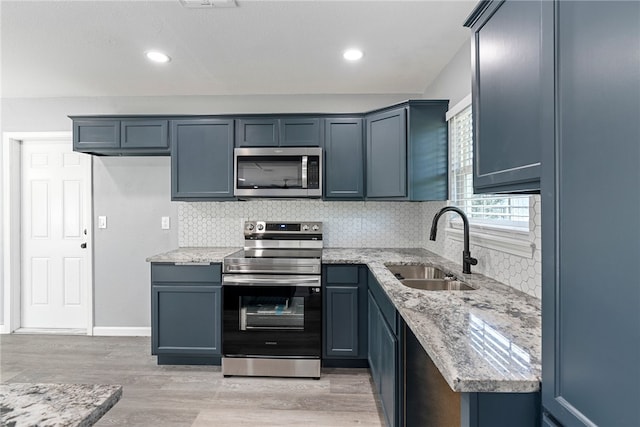 kitchen with appliances with stainless steel finishes, sink, light hardwood / wood-style flooring, and light stone countertops