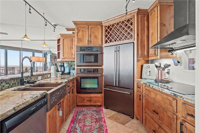 kitchen featuring wall chimney exhaust hood, sink, light stone counters, pendant lighting, and stainless steel appliances