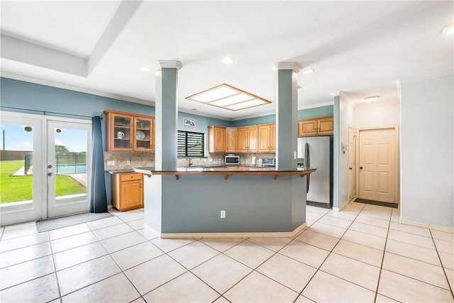 6041 King Trl, Corpus Christi, TX 78414 - kitchen featuring stainless steel fridge, a breakfast bar area, backsplash, crown molding, and light tile patterned floors