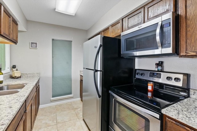 kitchen featuring light stone counters, sink, appliances with stainless steel finishes, and light tile patterned flooring