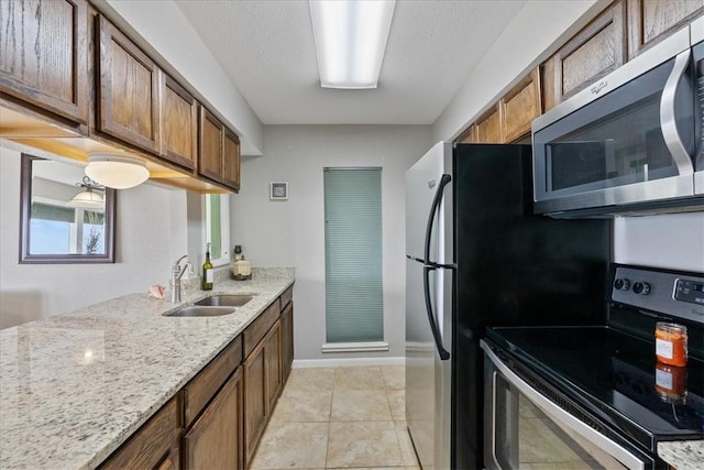 kitchen with a textured ceiling, stainless steel appliances, sink, light stone counters, and light tile patterned floors