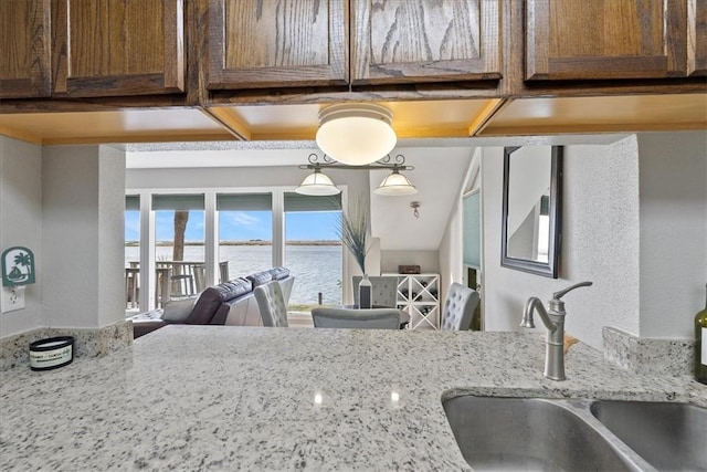 kitchen with a water view, light stone counters, and sink