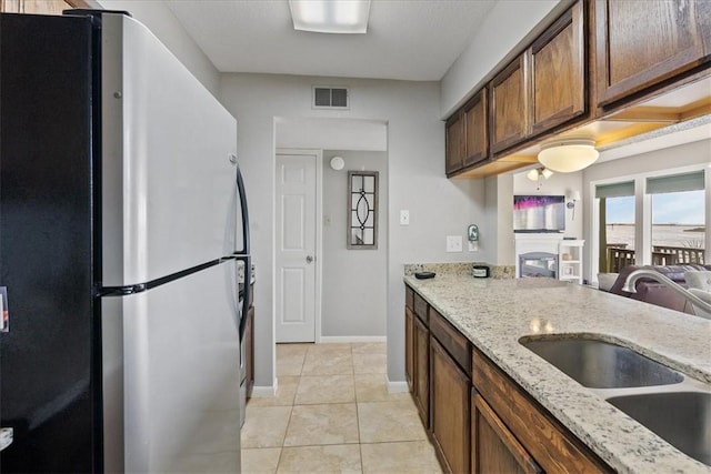 kitchen featuring light tile patterned flooring, sink, light stone countertops, and stainless steel refrigerator