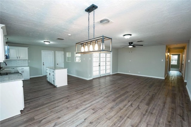 interior space featuring dark wood-style floors, backsplash, white cabinetry, a sink, and a kitchen island