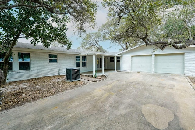 single story home with a garage, central AC, brick siding, and driveway