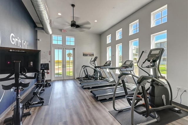 exercise room featuring ceiling fan, hardwood / wood-style floors, a wealth of natural light, and a towering ceiling