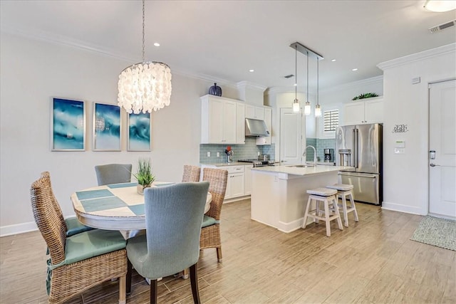 dining room featuring a notable chandelier, sink, ornamental molding, and light hardwood / wood-style flooring