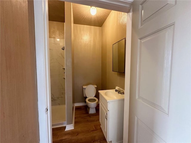 bathroom featuring toilet, vanity, wood-type flooring, and tiled shower