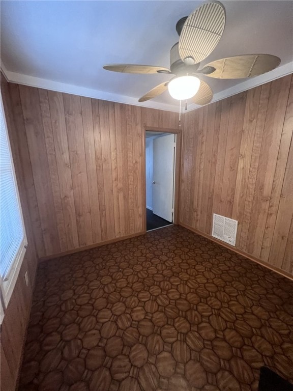 unfurnished room with ceiling fan and wood walls