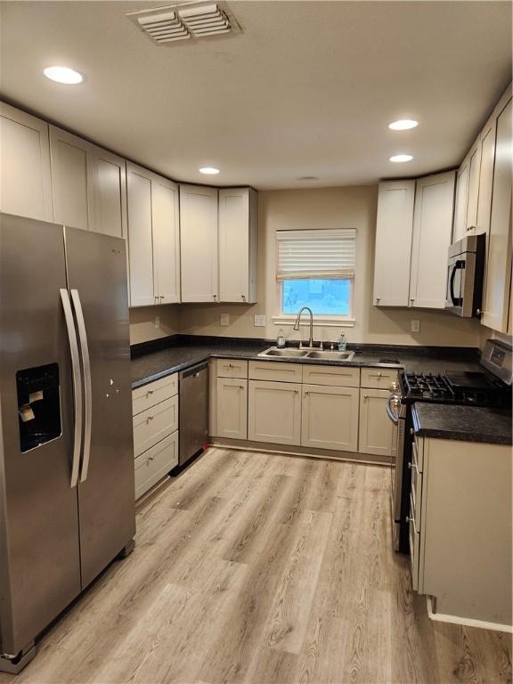 413 S 13th St, Aransas Pass, TX 78336 - kitchen featuring stainless steel appliances, a sink, dark countertops, light wood-style floors, and recessed lighting