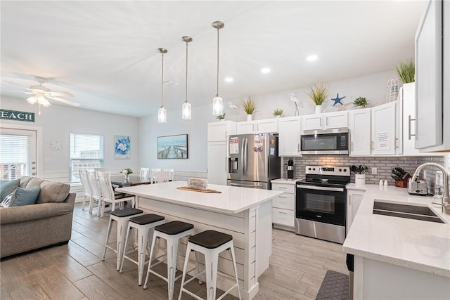 kitchen with sink, appliances with stainless steel finishes, white cabinetry, hanging light fixtures, and a center island