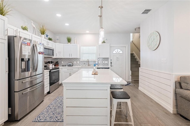 kitchen with stainless steel appliances, white cabinetry, a kitchen island, and decorative light fixtures