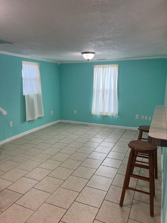 tiled empty room with ornamental molding and a textured ceiling