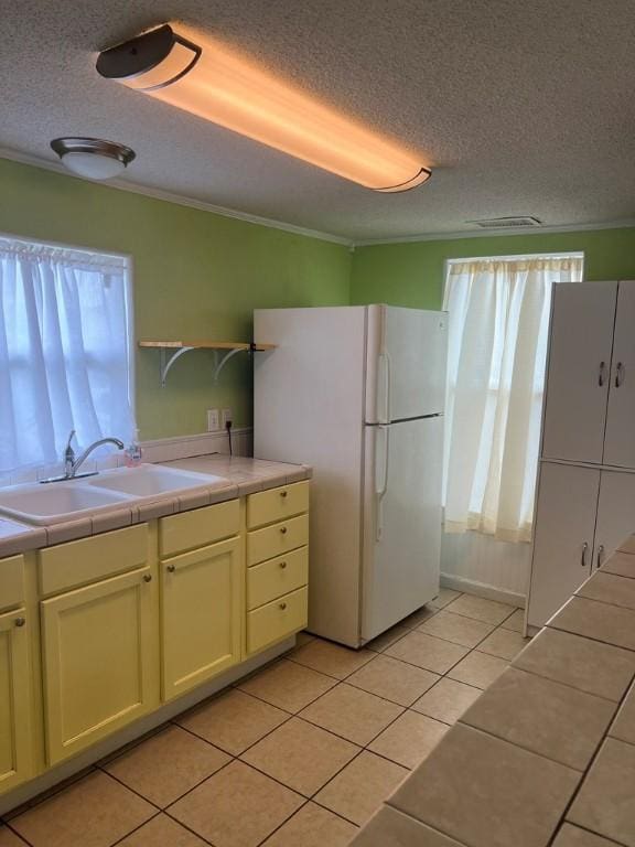 kitchen featuring tile countertops, sink, white fridge, and a healthy amount of sunlight