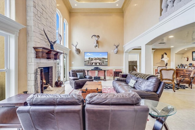 living room with a stone fireplace, a towering ceiling, and ornamental molding