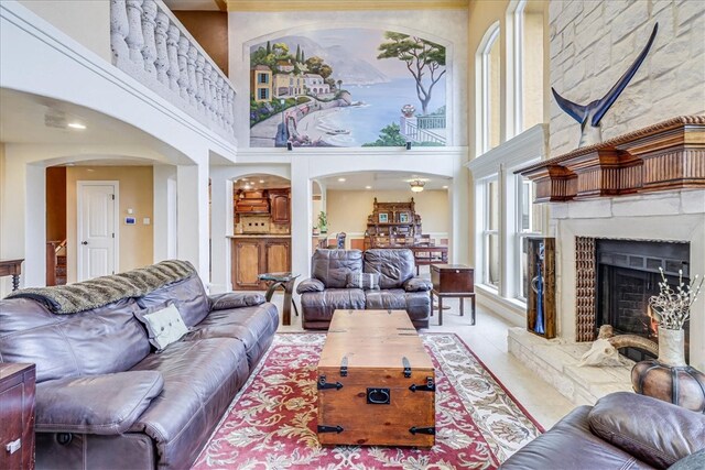 living room featuring a stone fireplace, a healthy amount of sunlight, and a high ceiling