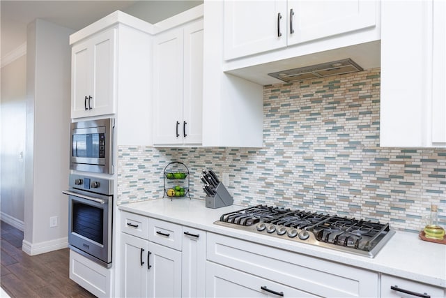 kitchen with appliances with stainless steel finishes, dark hardwood / wood-style flooring, tasteful backsplash, and white cabinetry