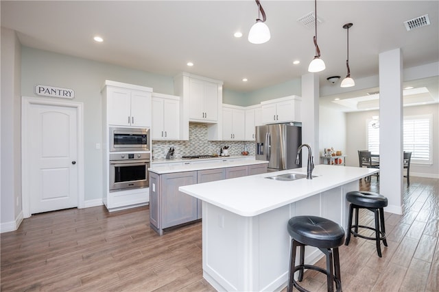 kitchen with sink, hanging light fixtures, stainless steel appliances, light hardwood / wood-style flooring, and a kitchen island with sink