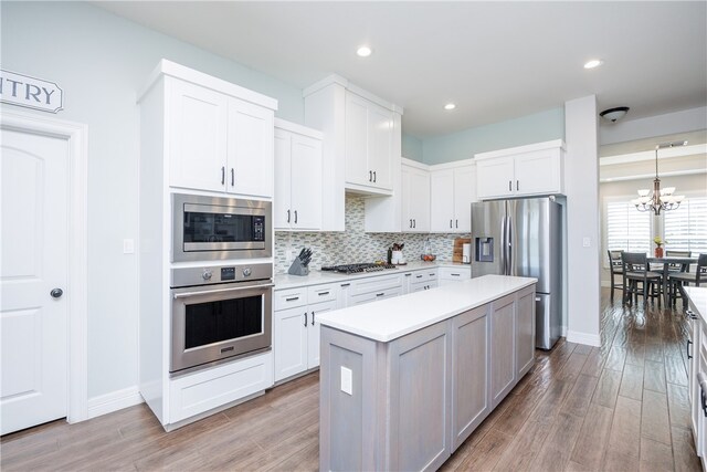 kitchen featuring stainless steel appliances, an inviting chandelier, a center island, light hardwood / wood-style floors, and white cabinetry