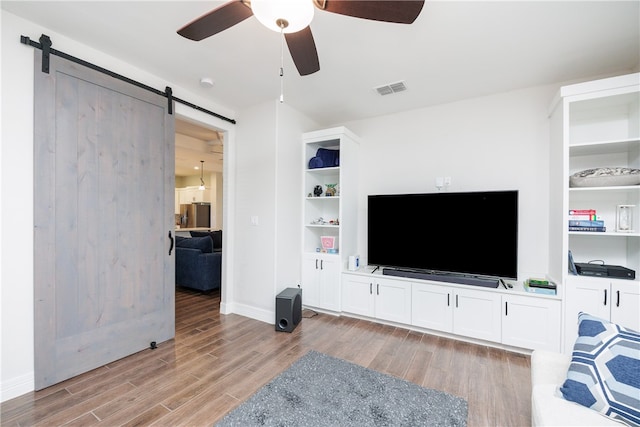 living room with a barn door, ceiling fan, and light hardwood / wood-style floors