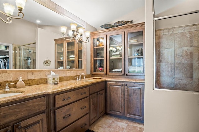 bathroom featuring a sink, double vanity, a notable chandelier, and a shower with shower door