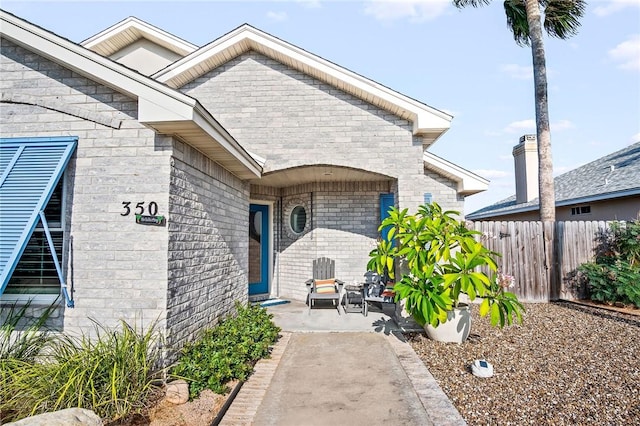doorway to property featuring brick siding, fence, and a patio area