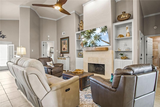 tiled living room with built in shelves, a high ceiling, ornamental molding, a ceiling fan, and a fireplace