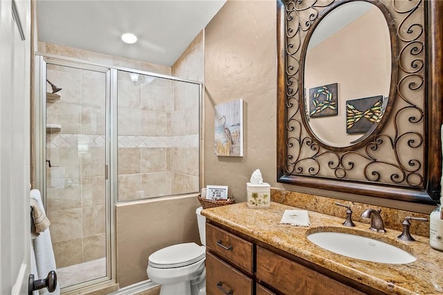 bathroom with a textured wall, toilet, vanity, and a stall shower