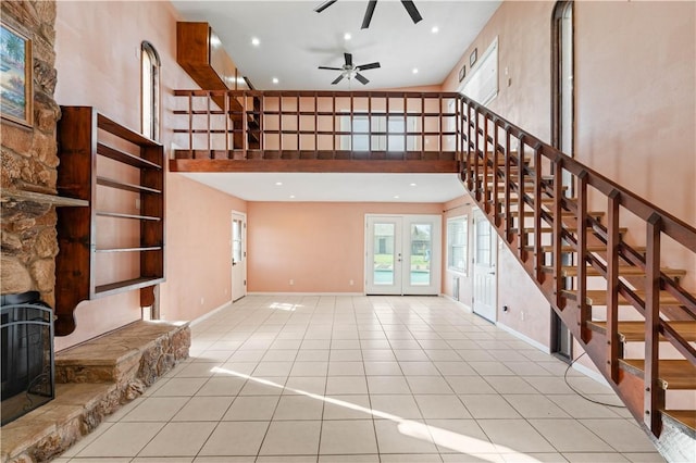 unfurnished living room with light tile patterned flooring, a high ceiling, baseboards, stairs, and french doors