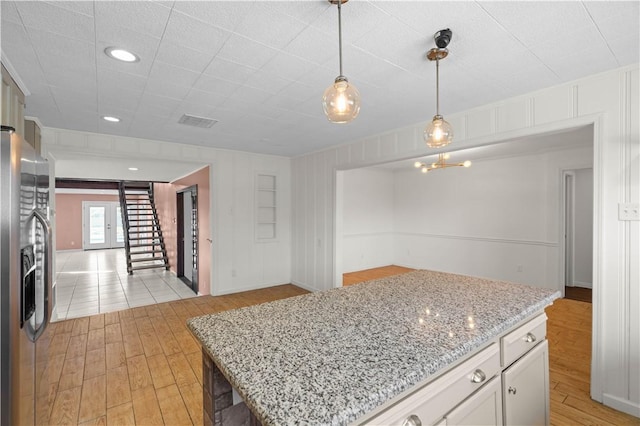 kitchen with visible vents, pendant lighting, light stone countertops, light wood-type flooring, and stainless steel refrigerator with ice dispenser