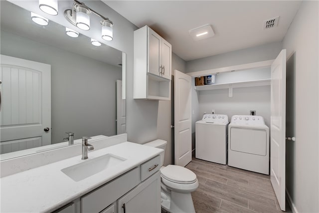 bathroom featuring washing machine and clothes dryer, wood-type flooring, vanity, and toilet