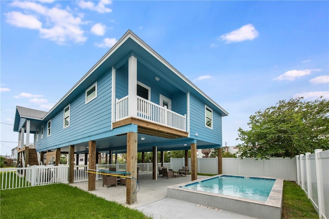 rear view of property featuring a fenced in pool, a patio, a yard, and a balcony