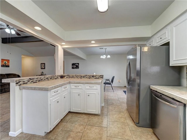 kitchen with kitchen peninsula, appliances with stainless steel finishes, decorative backsplash, ceiling fan with notable chandelier, and white cabinetry