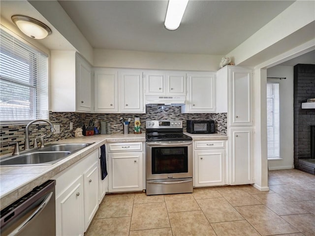 kitchen featuring white cabinetry, sink, stainless steel appliances, a fireplace, and light tile patterned floors