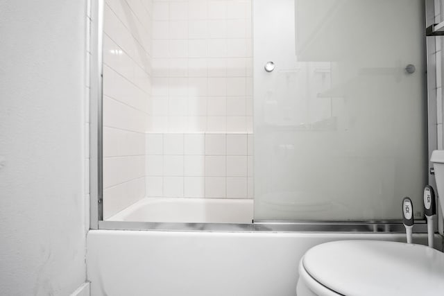 bathroom featuring combined bath / shower with glass door and toilet