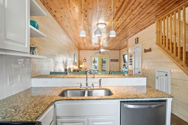 kitchen with pendant lighting, wood walls, stainless steel dishwasher, and sink