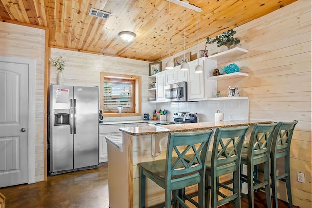 kitchen with appliances with stainless steel finishes, wood walls, a breakfast bar, white cabinets, and kitchen peninsula