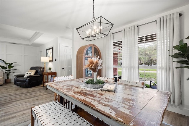 dining room featuring a raised ceiling, light wood finished floors, and a notable chandelier