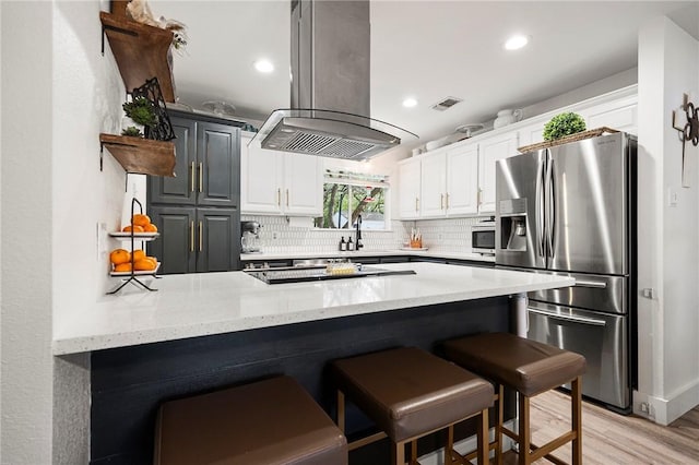 kitchen featuring visible vents, a peninsula, island range hood, stainless steel refrigerator with ice dispenser, and light stone counters
